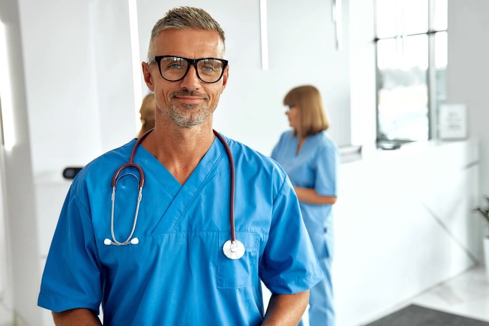 Smiling male doctor with glasses in blue scrubs and stethoscope | Find a Doctor Near You in Cappadocia | Online Doctor | E-rx.online